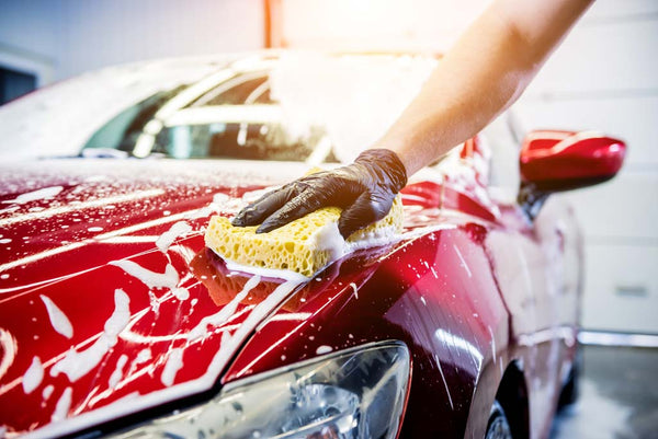 A hand washing a car with a soapy sponge