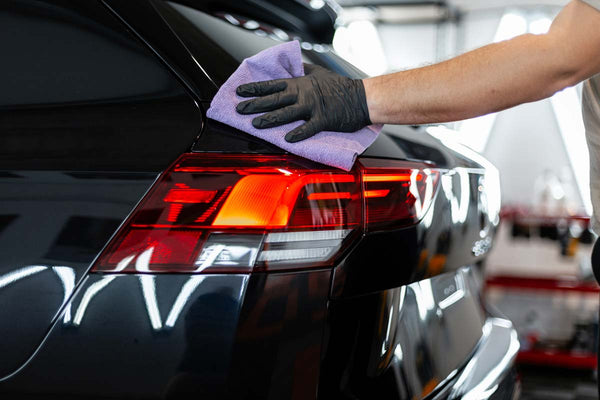 A hand washing a black car with a cloth