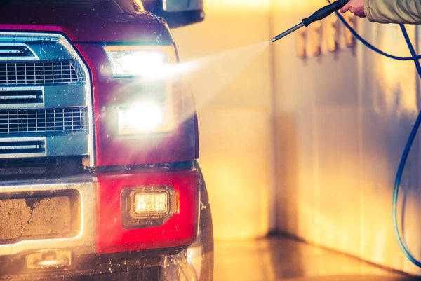 A man using a pressure washer to clean the front of a truck.
