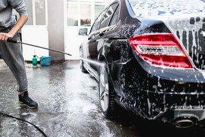 Someone spraying a soapy car with a power washer