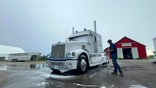 Todd founder of Image Wash Products washing a blue semi truck on a farm.
