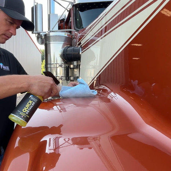 Man holding spray bottle of Quick Detailer spraying and wiping on semi truck fender