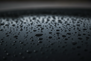 up close dark black shiny metal vehicle surface with water drops on it. Dark.